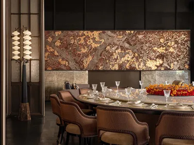 Dining room with a round table set with wine glasses, cups, and bowls, surrounded by chairs, in a room with a marble-textured wall and dim warm lighting