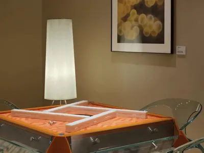 A well-lit living room with a glass dining table, two chairs, a couch, and a lamp, featuring glass and wood materials
