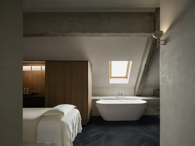 Bright and airy bedroom with a white color scheme, a bed near the window, and a bathtub in the corner