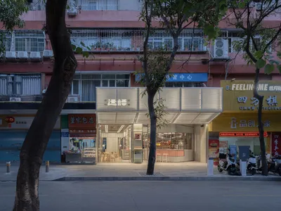 一間擁有玻璃混凝土立面的大型窗戶與門的現代餐廳，背景為樹木與柔和的漫射燈光
