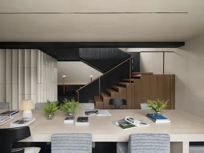 A well-lit living room with a dining table, chairs, and a staircase, featuring a cozy and inviting atmosphere with books and magazines scattered on the table