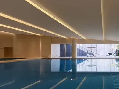 A relaxing pool area with a hotel building in the background, surrounded by a deck and chairs, inviting guests to unwind