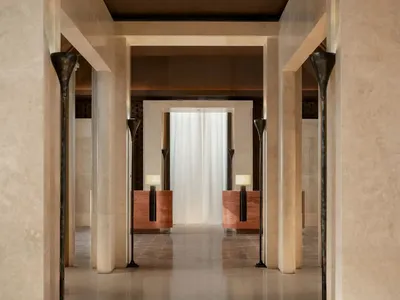 A dimly lit hotel hallway with white marble floors and walls, featuring two lamps on the floor for lighting