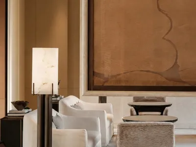 A well-lit living room with a couch, chair, and dining table, featuring a brown wall hanging and a warm atmosphere