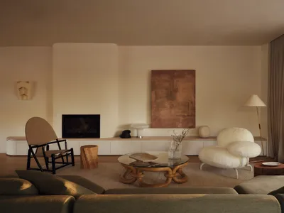 A well-lit living room with a white couch, a chair, and a fireplace, surrounded by a dining table and a lamp