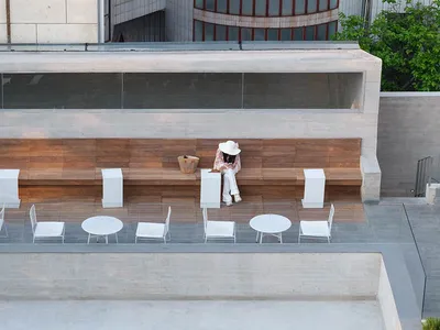 A casual outdoor restaurant with wooden furniture, a woman sitting on a bench, and other people in the scene