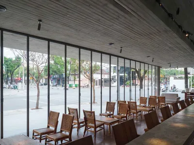A modern restaurant space with wood furniture, high ceilings, and large windows allowing natural light to flood the area