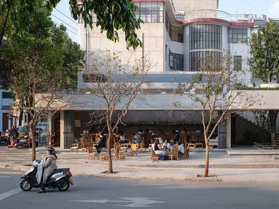 Outdoor restaurant with modern design, wood, and concrete elements, surrounded by people sitting at tables in a casual and relaxed atmosphere