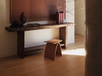 A well-lit living room with a wooden floor, a wooden table, a chair, and a potted plant, creating a warm and inviting atmosphere