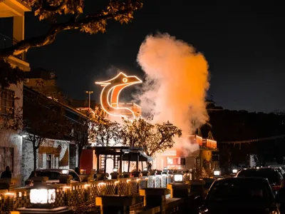 A restaurant building at night with a large illuminated bird statue on top, surrounded by dining tables and chairs