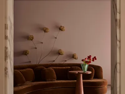 Cozy modern living room with a brown couch and chair, a vase with flowers on a table, and dim lighting