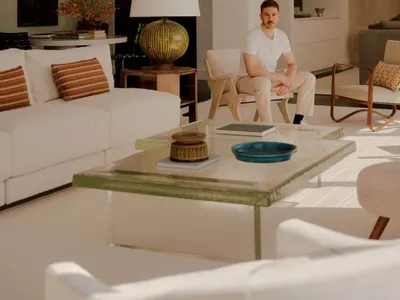 A well-furnished living room with a man sitting on a chair, surrounded by a couch, dining table, and vase, with a comfortable atmosphere