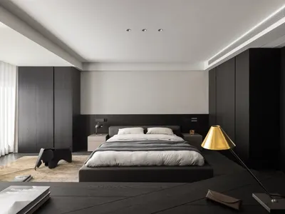 A dimly lit hotel bedroom with a black bed, chair, and gold lamp, creating a cozy atmosphere