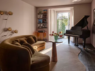 A dimly lit living room with a piano, couch, chair, dining table, and vases, featuring wood and fabric materials in a predominantly neutral color palette