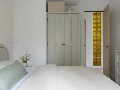 A minimalist bedroom with a bed, dresser, and closet, featuring a white comforter, two potted plants, and a clean, organized space