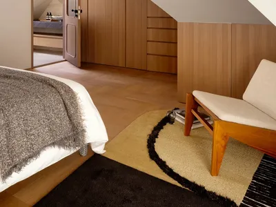 Cozy bedroom with a bed, chair, and couch, featuring wooden furniture and a rug, with natural lighting creating a warm atmosphere