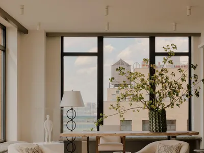 Cozy living room with a large window, a couch, chairs, and a dining table, surrounded by a potted plant, in a well-lit space
