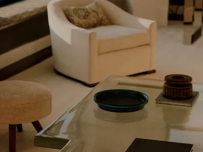A well-lit living room with a glass coffee table, a couch, a chair, and a book, creating a cozy atmosphere
