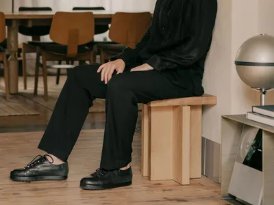 一名男子坐在木質長椅上，置身於溫馨客廳，地板與牆面皆為木質，另有餐桌椅組