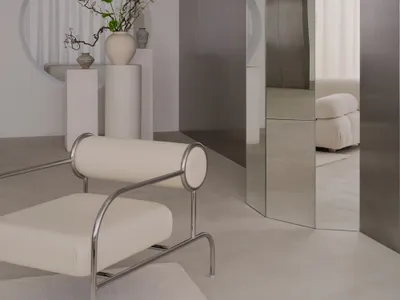 A modern living room with a large mirror, a couch, a chair, and a potted plant, featuring white and grey tones and soft inviting lighting