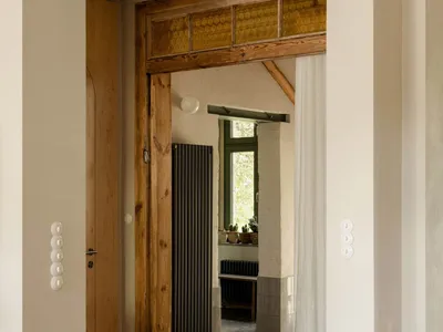 A modern kitchen with a wooden floor, a white door, and natural light from the open doorway