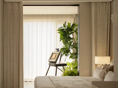 A well-lit bedroom with a bed, a potted plant, and a painting on a stand, surrounded by white curtains and wood accents