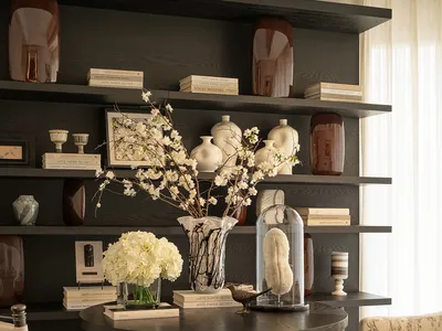 Cozy modern living space with a black table, vase of flowers, bookshelf, chair, couch, and natural light from windows