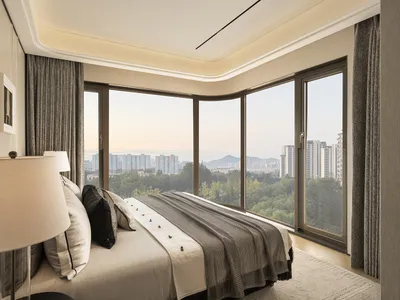 Cozy bedroom with a striped bed, a lamp, and a chair, featuring a large window with a city view and natural light