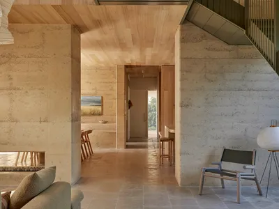Cozy living room with a couch, chair, and dining table on a wooden floor, near a staircase, with natural light from windows