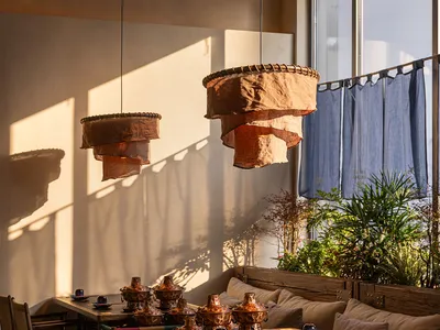 A dining area with a wooden table, chairs, and potted plants, set with plates, bowls, and cups, in a warm and inviting atmosphere with natural light from the windows