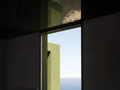A well-lit living room with a couch and chair in front of a large ocean-facing window, featuring a mix of wood and metal furniture and decor