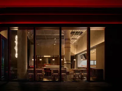 A modern restaurant interior with dining tables, chairs, and benches in a neutral color palette, with warm and soft lighting