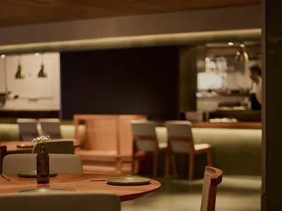 A dimly lit restaurant dining area with a large wooden table and metal chairs, surrounded by plates, bowls, and a vase, creating a warm and inviting atmosphere