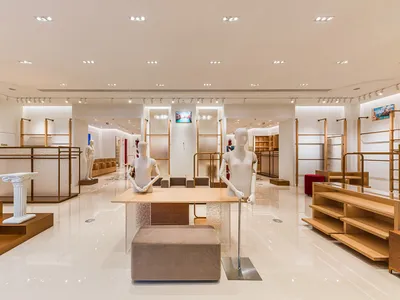寬敞的奢華零售展示間，設有淺橡木服裝展示架、白色人體模型、拋光大理石地板與嵌入式天花板燈光。