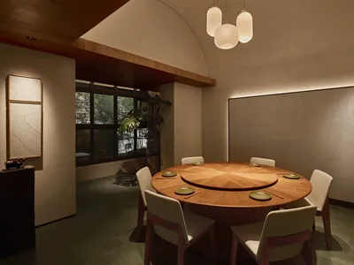 Modern minimalist dining room with a large round oak table, six upholstered chairs, curved wooden ceiling detail, and textured wall with topographic lines.
