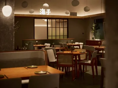 現代日式餐廳內部，木質餐桌、布面與藤編靠背椅、混凝土柱，以及溫暖吊燈，後方牆面有發光中文字。