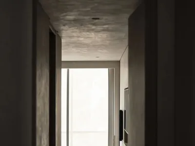 View through a doorway into a minimalist concrete hallway featuring a woven lounge chair, black side table, and large window with natural light.