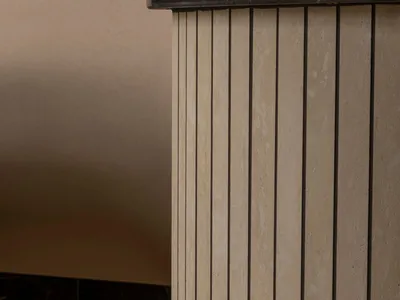 Close-up of a fluted travertine cabinet featuring vertical grooves and a dark marble countertop against a neutral textured wall.