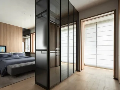 現代臥室室內設計，胡桃木主牆、深藍色寢具、黑色金屬邊框玻璃衣櫃，以及床尾灰色軟墊長凳。