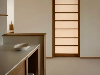 極簡風室內空間，畫面中央為直立式橡木拉門，門上有水平半透光面板並由後方暖光照亮，前景有木質檯面與白色碗。