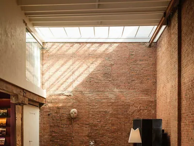 寬敞的工業風loft客廳，擁有全高裸露紅磚牆、橄欖綠模組化天鵝絨沙發、淺色木地板，以及上方的大型天窗。