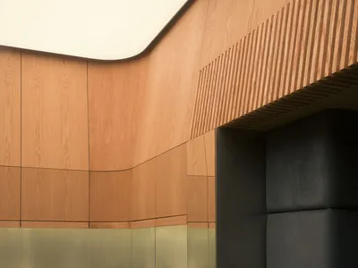 Interior view of a luxury jewelry store featuring curved walnut wood paneling, backlit glass display cases, and dark green marble tile flooring with padded dark wall panels.