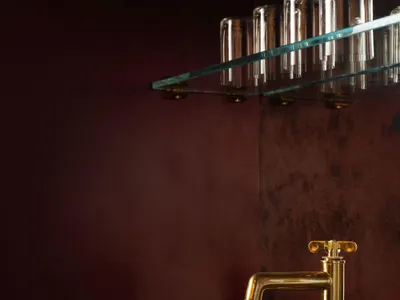 Close-up of a luxury bathroom vanity with deep burgundy marble countertop and integrated sink, paired with a polished brass faucet against a matching burgundy wall and glass shelf above.