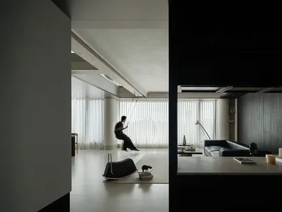 現代極簡客廳，設有懸吊室內鞦韆、微水泥牆面與天花板、深色木質板材，以及在柔和自然光下的黑色皮革沙發。
