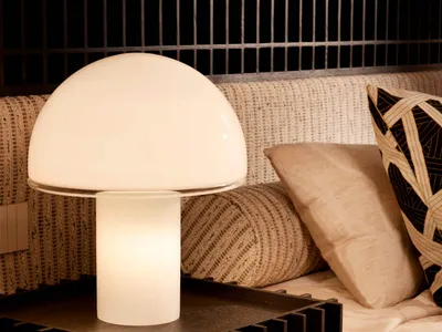 Close-up of a modern white mushroom table lamp on a dark oak grid-patterned bedside table, with neutral textured pillows and woven bedding in the background.