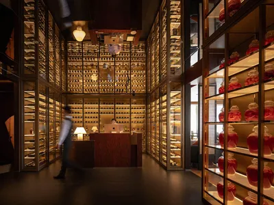 Luxurious modern wine cellar interior featuring floor-to-ceiling brass and glass shelving filled with wine bottles and preserved delicacies, warm ambient lighting, and a central service counter.