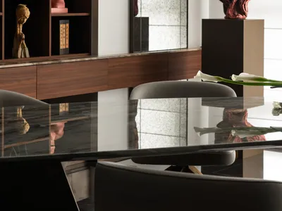 Modern dining room featuring a dark walnut built-in cabinet displaying Chinese art pieces, a large textured mirror, and a dramatic red stone sculpture on a pedestal, with a glossy black dining table in the foreground.