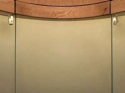 Jewelry displayed on dark textured volcanic stone arch-shaped stands inside a modern curved glass and wood display cabinet with integrated lighting.