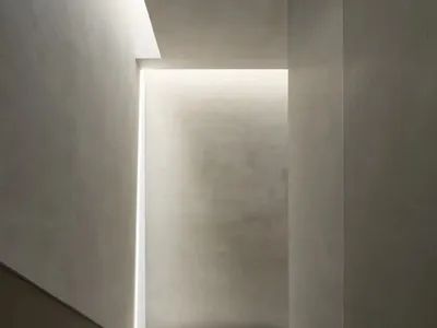 俯視極簡混凝土樓梯，牆面與天花板嵌入連續線性LED燈帶提供照明。