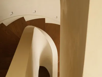 View looking down a modern curved staircase featuring smooth off-white plaster walls and balustrade paired with dark oak wooden treads and recessed ceiling lighting.